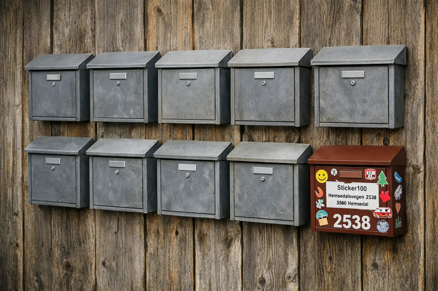 Row of metal mailboxes on a wooden wall with one colorful mailbox to the right.